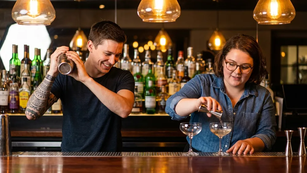Cocktailkurs in Berlin – Zwei Personen mixen Cocktails an einer Bar unter Anleitung