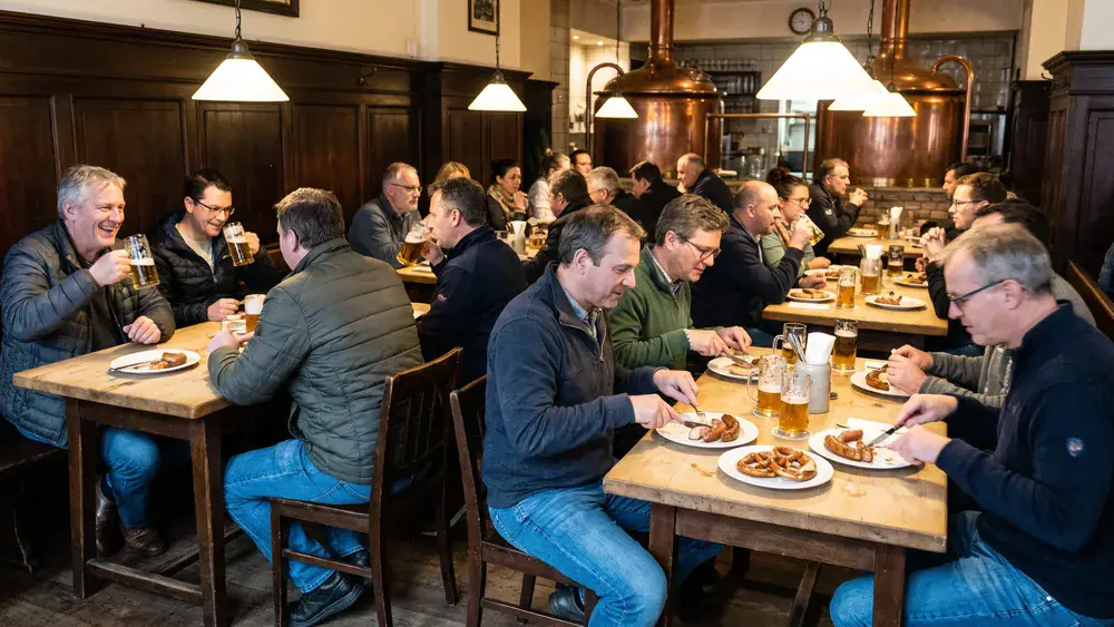 Brauhaus in Bielefeld – Kollegen trinken Hausbier an langen Tischen mit Kupferkesseln im Hintergrund in der Altstadt