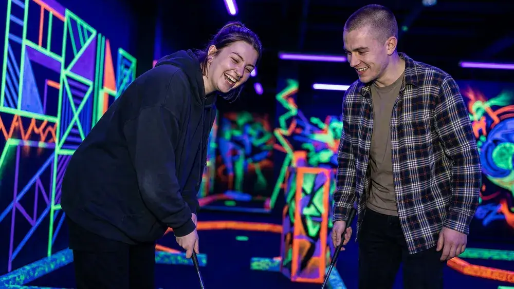 GolfZone Schwarzlicht Minigolf in Bielefeld – Zwei Personen spielen am Sonntag im Neonlicht