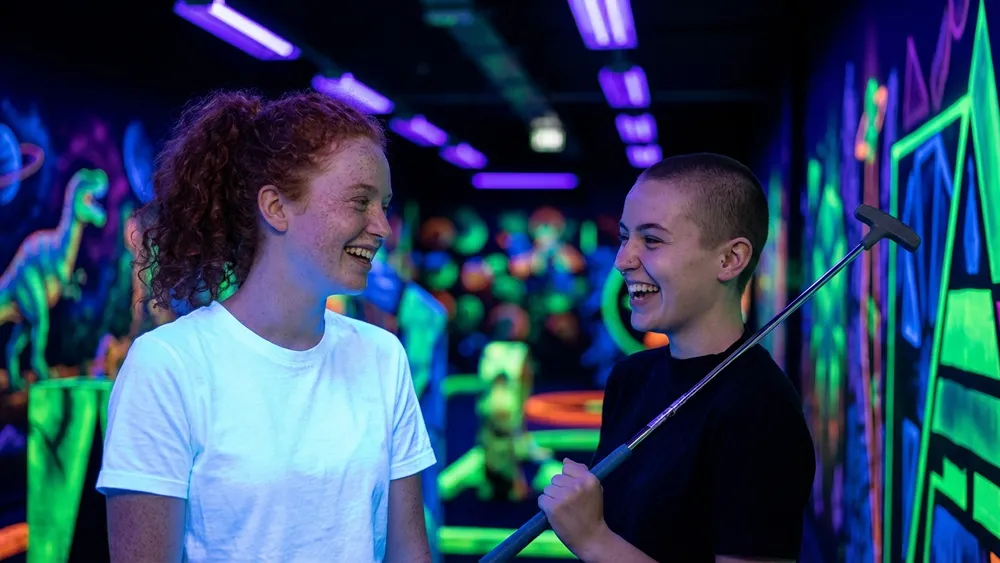 Schwarzlichtlöwen Minigolf in Braunschweig – zwei Personen spielen Minigolf unter UV-Licht
