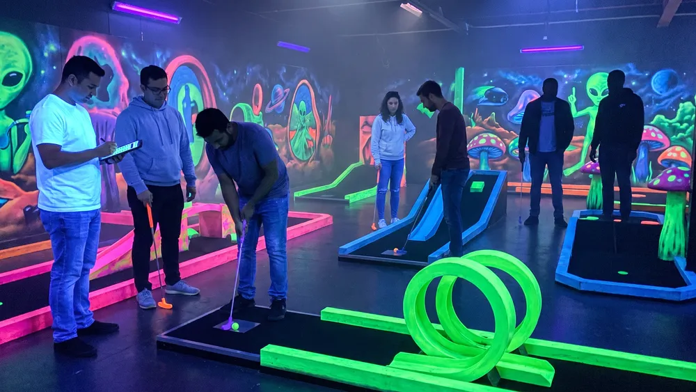Schwarzlicht Minigolf in Braunschweig – Kollegen spielen Minigolf unter UV-Licht zwischen leuchtenden Graffiti-Wänden