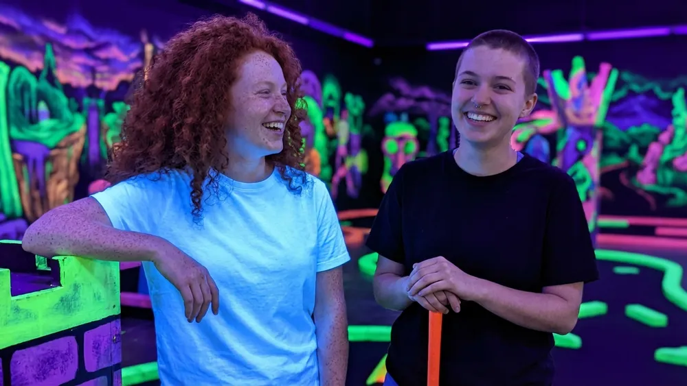 Schwarzlicht Minigolf in Braunschweig – Team spielt Minigolf unter UV-Licht zwischen leuchtenden Graffiti-Wänden