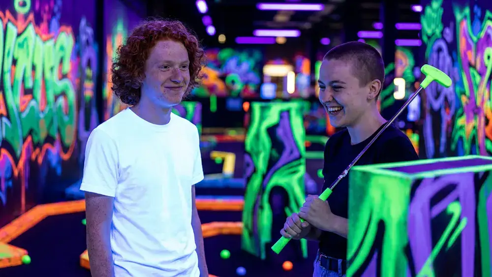 Schwarzlichtlöwen Minigolf in Braunschweig – zwei Personen spielen Minigolf unter UV-Licht