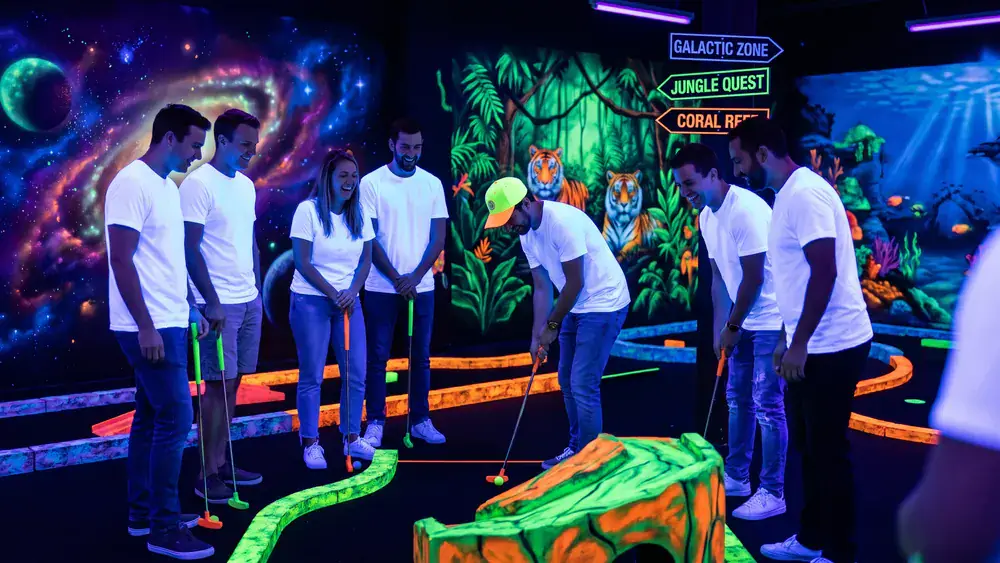 Schwarzlicht Minigolf in Braunschweig – Kollegen spielen Minigolf unter UV-Licht zwischen leuchtenden Graffiti-Wänden