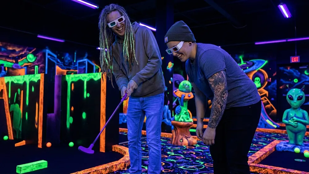Glowing Rooms in Dortmund – Zwei Personen spielen Schwarzlicht-Minigolf mit 3D-Brillen