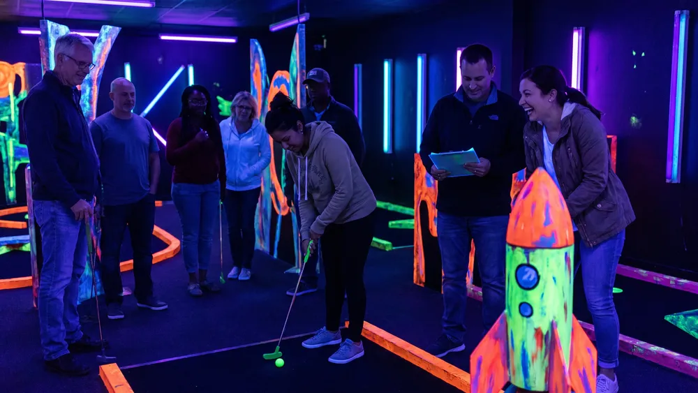 Schwarzlicht Minigolf in Düsseldorf – Kollegen spielen Minigolf in leuchtender Neonwelt