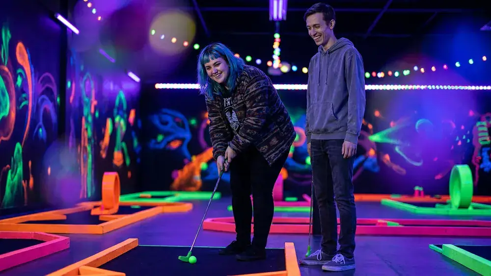 Glowzone Schwarzlicht Minigolf in Düsseldorf – Zwei Personen spielen in leuchtender 3D-Neonwelt