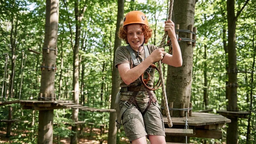 Hochseilgarten in Düsseldorf – Schüler klettert gesichert auf einer Plattform in den Baumwipfeln
