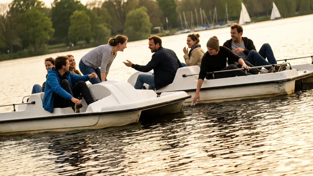 Tretboot auf der Alster in Hamburg – Kollegen paddeln lachend auf mehreren weißen Tretbooten über die Außenalster