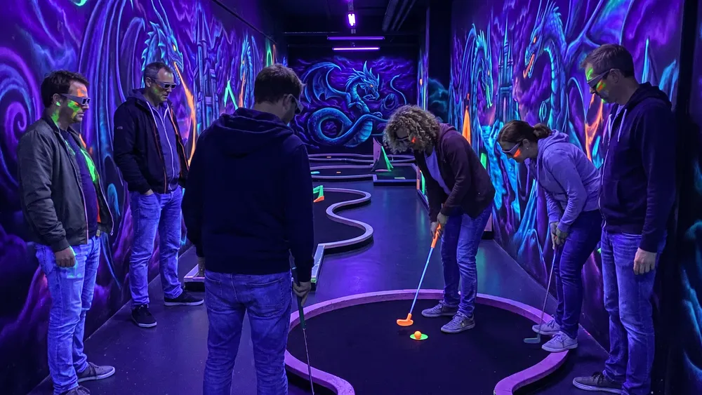 Schwarzlicht-Minigolf in Hamburg – Kollegen spielen mit 3D-Brillen unter Neonlicht in Stellingen