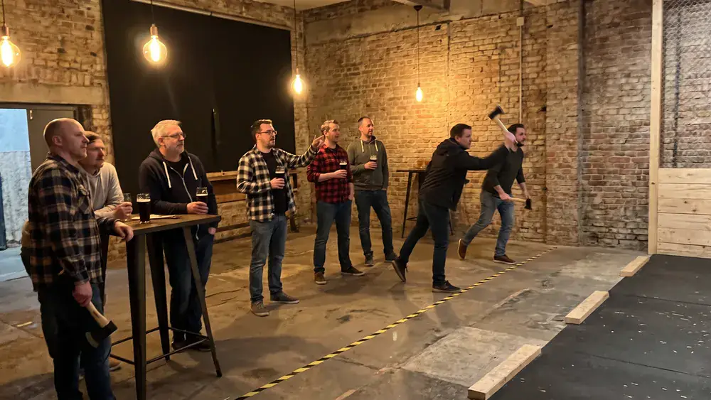 Axtwerfen in Hamburg – Kollegen werfen Äxte auf Holzscheiben in einer Industriehalle, Bier in der Lounge danach
