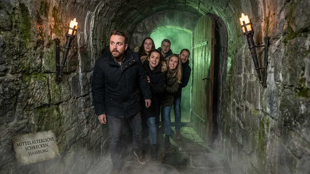 Hamburg Dungeon – Gruppe in einem dunklen mittelalterlichen Tunnel mit Fackellicht in der Speicherstadt