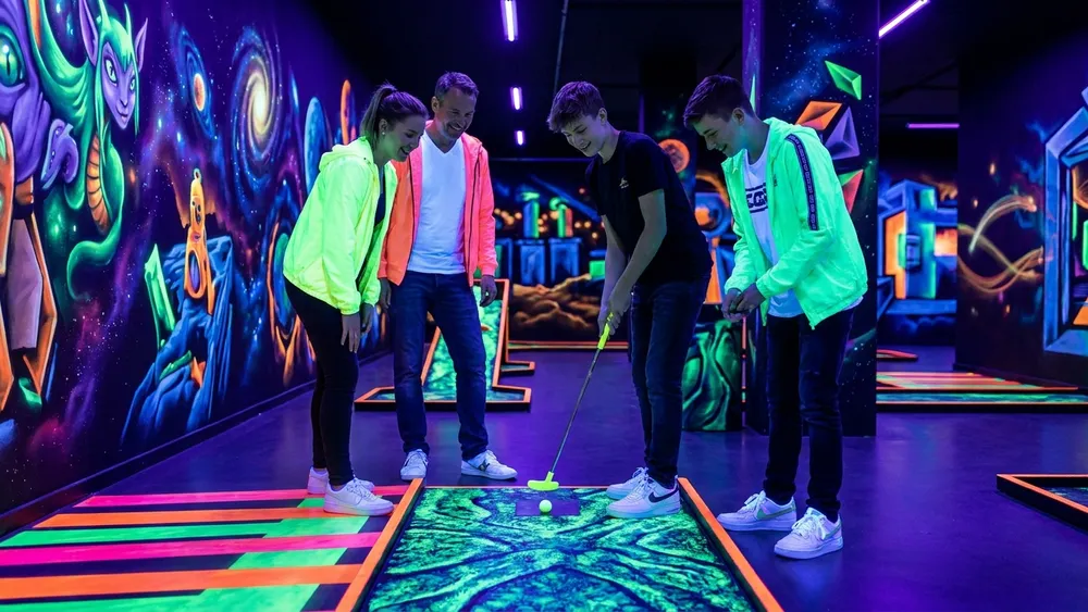 Schwarzlichtviertel Hamburg – Familie spielt UV-Minigolf vor leuchtenden 3D-Fantasy-Wandbildern