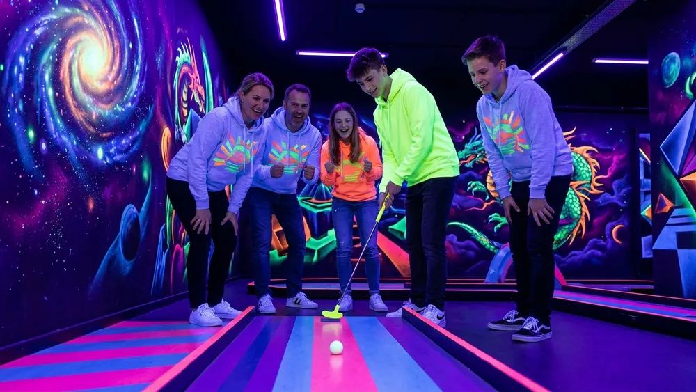 Schwarzlichtviertel Hamburg – Familie spielt UV-Minigolf vor leuchtenden 3D-Fantasy-Wandbildern