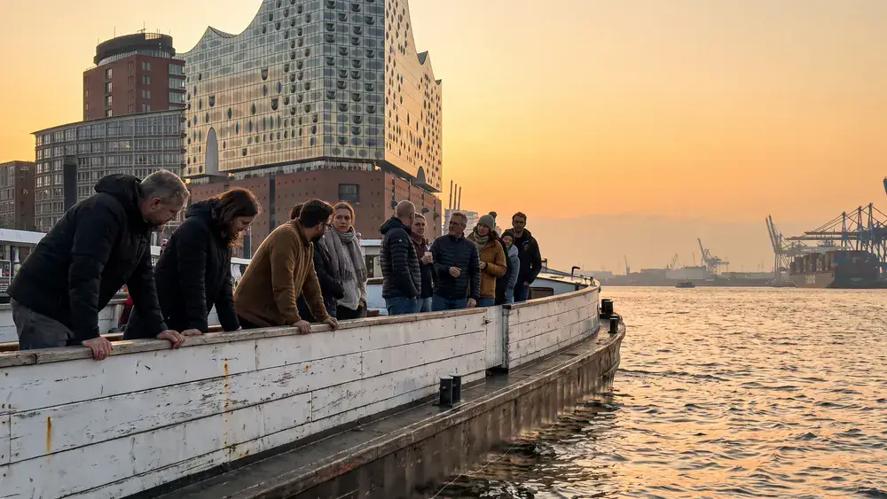 Hafenrundfahrt in Hamburg – Kollegen stehen an Deck einer Barkasse mit Elbphilharmonie im Hintergrund