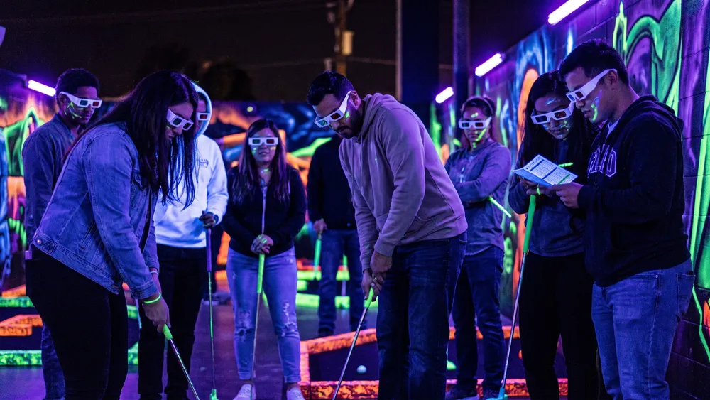 Schwarzlicht Minigolf in Hannover – Kollegen spielen mit 3D-Brillen Minigolf in leuchtender Neonwelt
