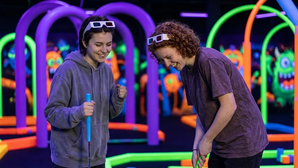 Schwarzlicht Minigolf in Hannover – Schüler spielen Minigolf auf leuchtenden Neon-Bahnen
