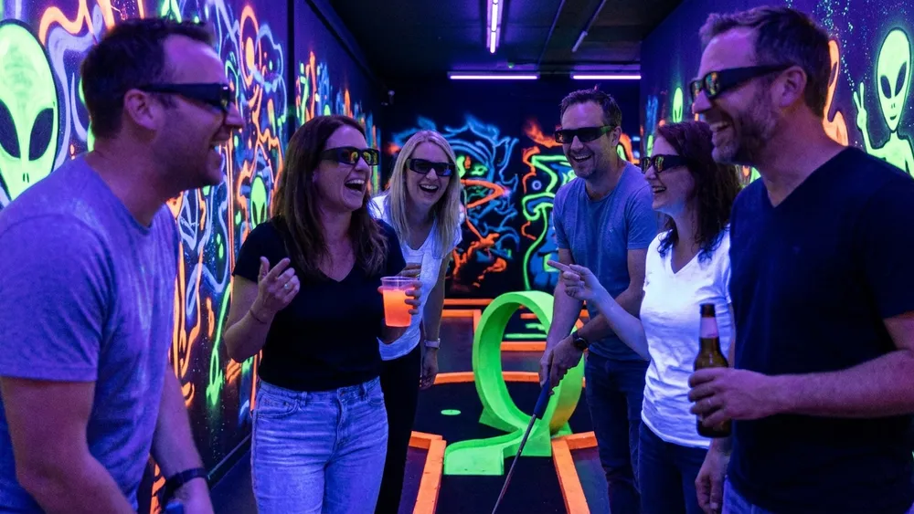 Schwarzlicht Minigolf in Köln - Erwachsene spielen mit 3D-Brille in leuchtenden Neonräumen