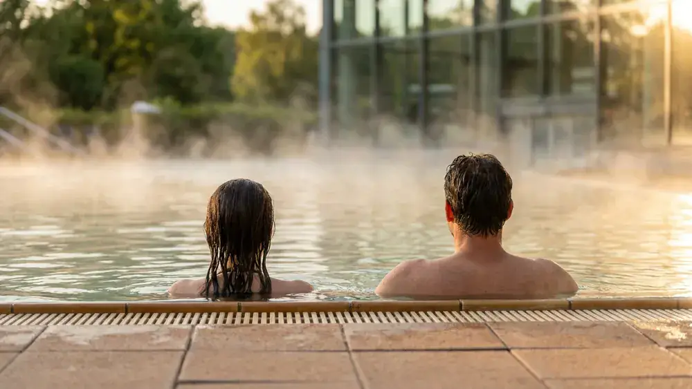 Claudius Therme in Köln – Zwei Personen entspannen im Thermalbecken mit Blick in den Rheinpark