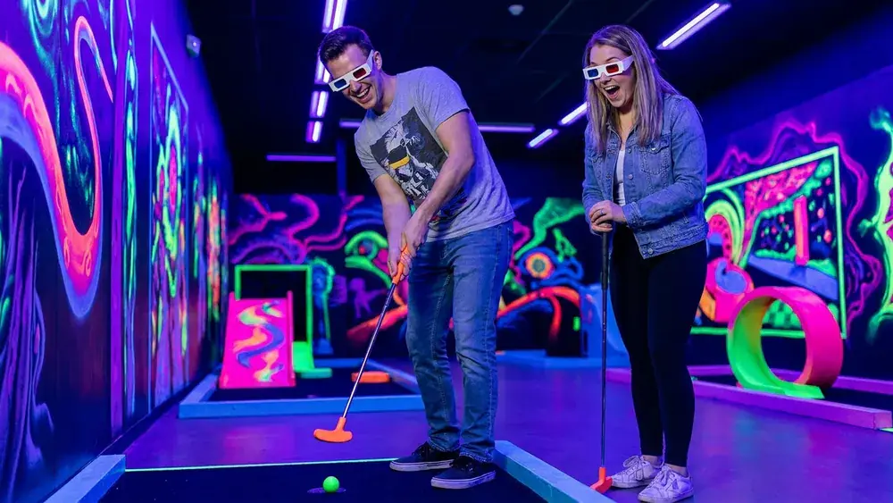 Schwarzlicht Minigolf in Köln – Zwei Personen spielen Minigolf in leuchtender 3D-Neonwelt