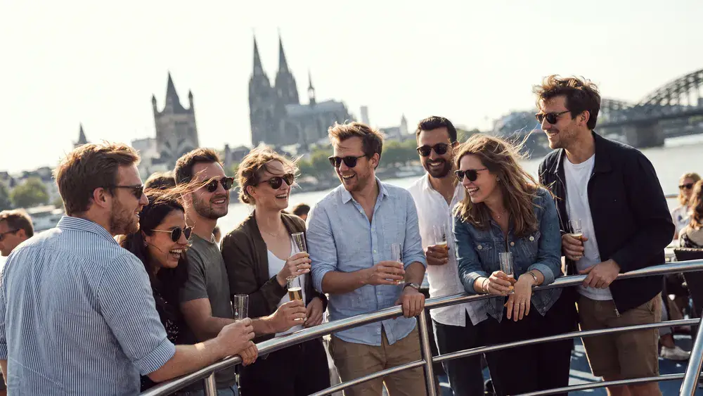 KD Panoramafahrt in Köln – Kollegen stehen an Deck eines Rheinschiffs mit Blick auf den Dom