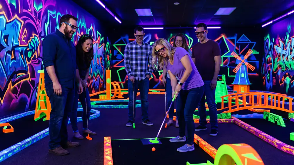 Schwarzlicht Minigolf in Köln – Kollegen spielen mit 3D-Brillen Minigolf in leuchtender Neonwelt