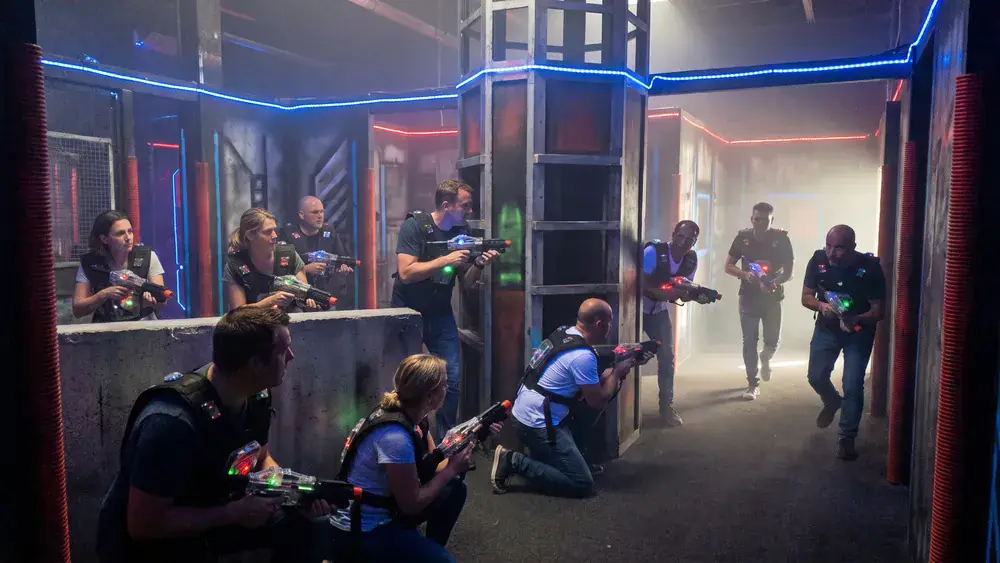 Lasertag in Stuttgart – Kollegen in Sensorwesten spielen als Gruppe mit Phasern in einer dunklen Neon-Arena