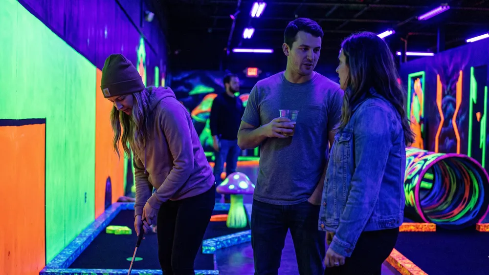 Schwarzlicht Minigolf in Stuttgart – Kollegen spielen als Gruppe mit 3D-Brillen Minigolf in leuchtender Neonwelt