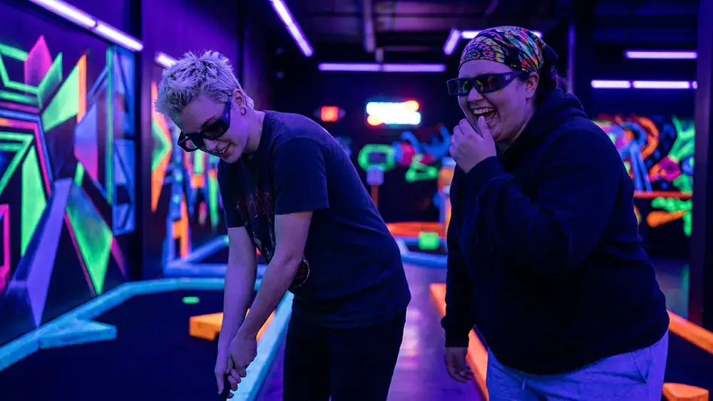 Blacklight Stuttgart – Zwei Personen spielen Schwarzlicht-Minigolf auf leuchtenden Neon-Bahnen