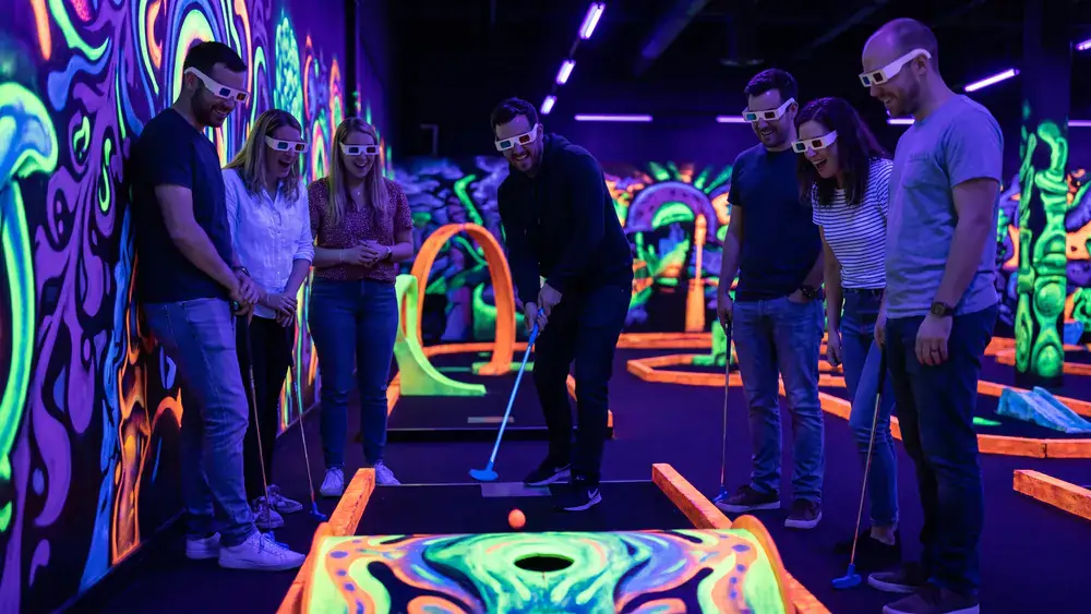 Schwarzlicht Minigolf in Stuttgart – Kollegen spielen mit 3D-Brillen Minigolf in leuchtender Neonwelt