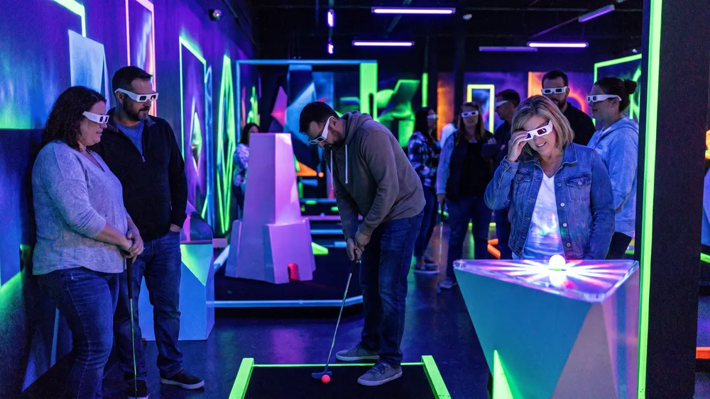 Schwarzlicht Minigolf in Wien – Kollegen spielen mit 3D-Brillen Minigolf in leuchtender Neonwelt