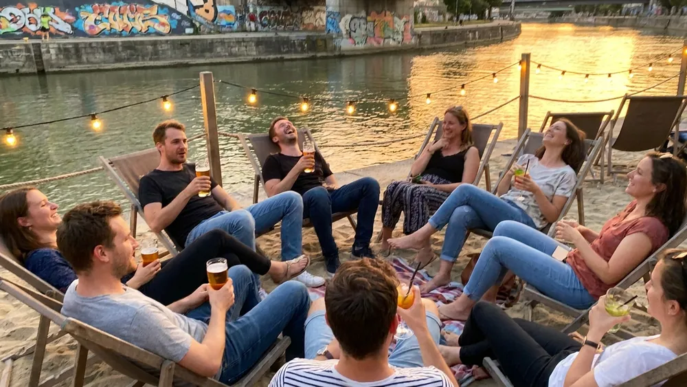 Donaukanal Wien – Gruppe sitzt mit Drinks am Sandstrand der Strandbar Herrmann