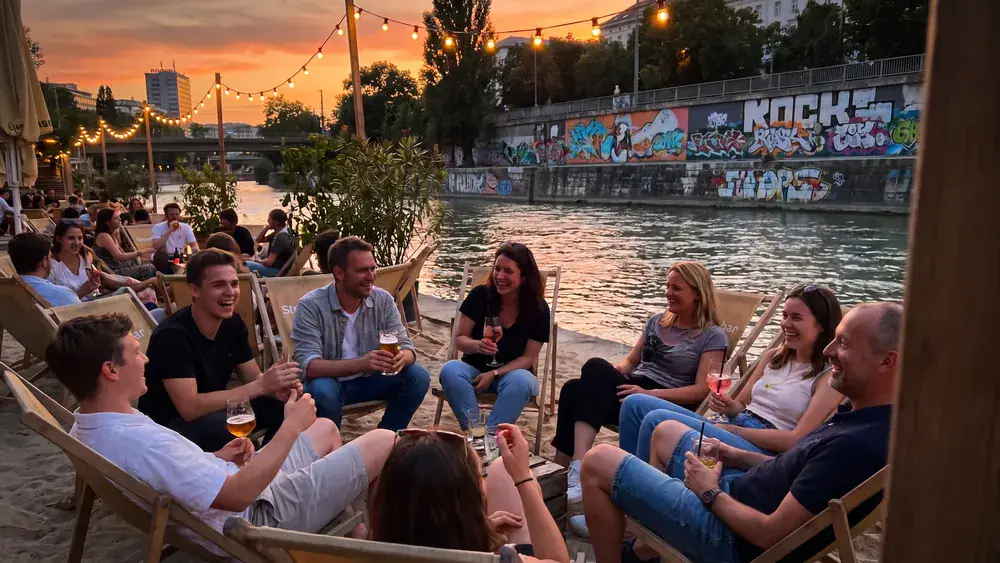 Donaukanal Wien – Kollegen sitzen mit Drinks am Sandstrand der Strandbar Herrmann