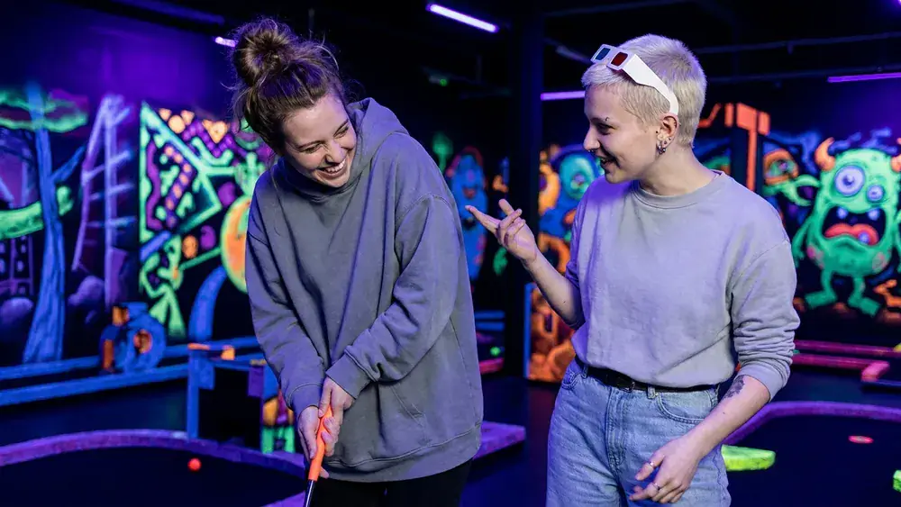 Schwarzlichtfabrik Würzburg – Zwei Personen spielen 3D-Minigolf unter Schwarzlicht